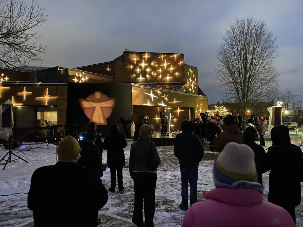 Celebration of Life 2020 - outside vigil with stars lite up against the Our Lady of Peace building. People lookiing at the building standing in the snow.
