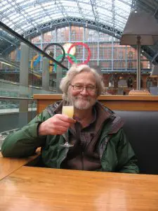 a picture of Jack Whitehurst, smiling, and holding a drink with the Olympic symbol behind him.