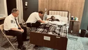 A navy chaplain blessing a former solder who is laying in bed resting.