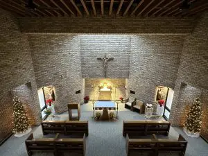 A picture of the Our Lady of Peace Chapel during Christmas. Two Christmas trees and 2 pointsettas.