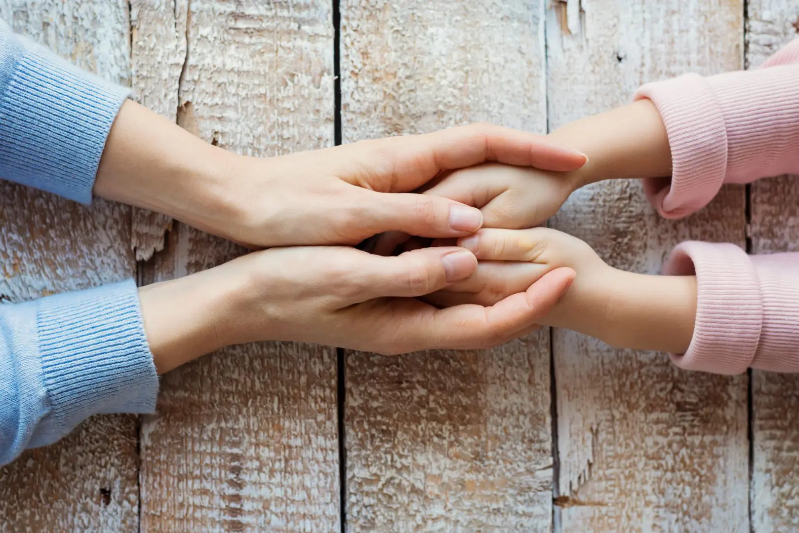 a wooden table with a two sets of hands being held. A young childs inside an adults hands