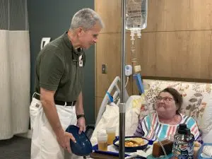 Tom-and-Patient-scaled - Our Lady of Peace Nurse, Tom is wearing an olive green shirt with white pants talking with a female patient who is getting ready to eat luch.