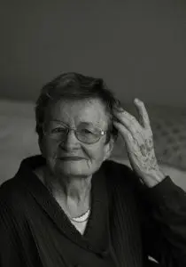 black and white photo of a women with short hair and glasses wearing a black sweater touching her hair