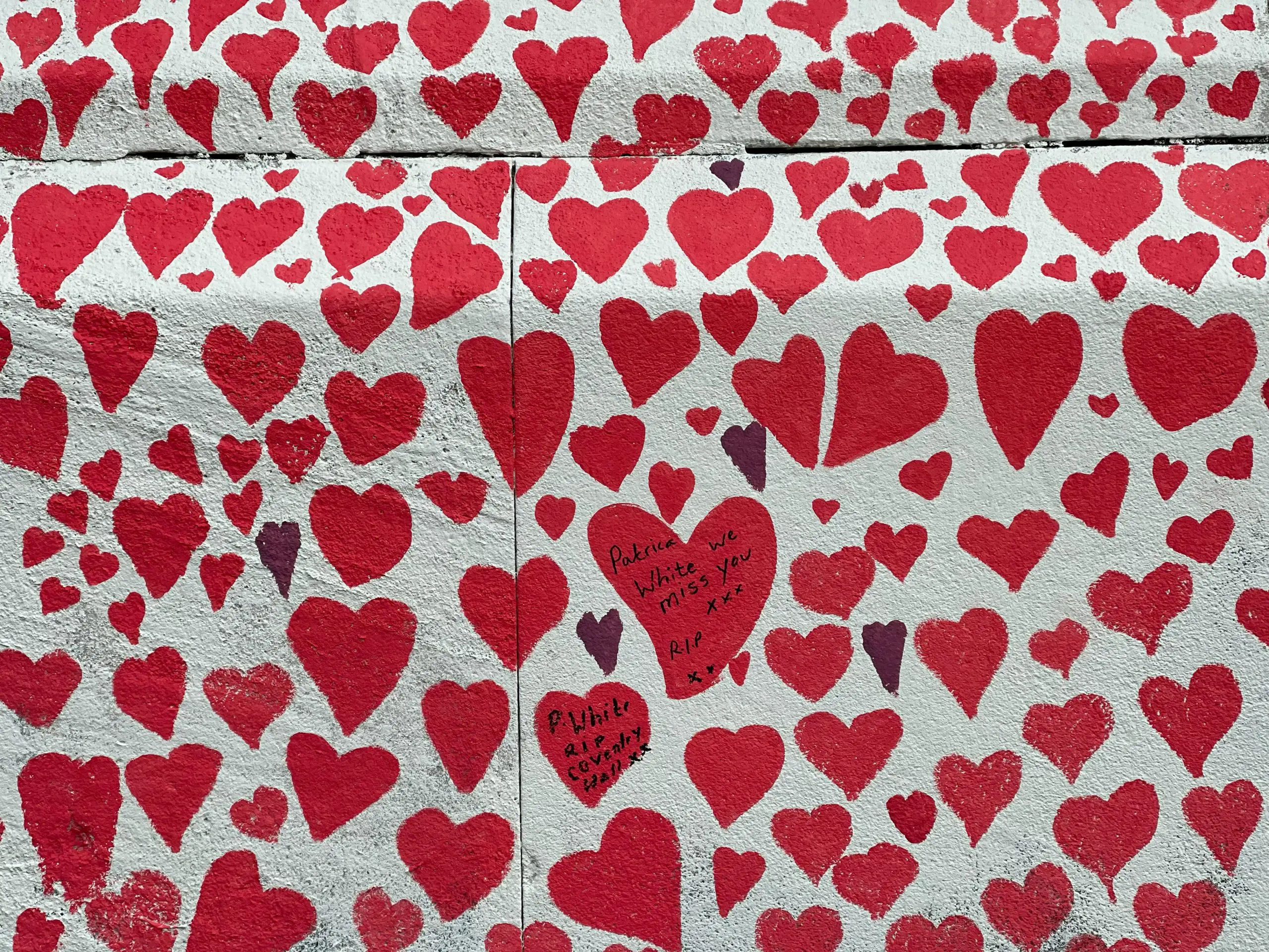 white wall with various sizes of red hearts painted all over it with a few black hearts