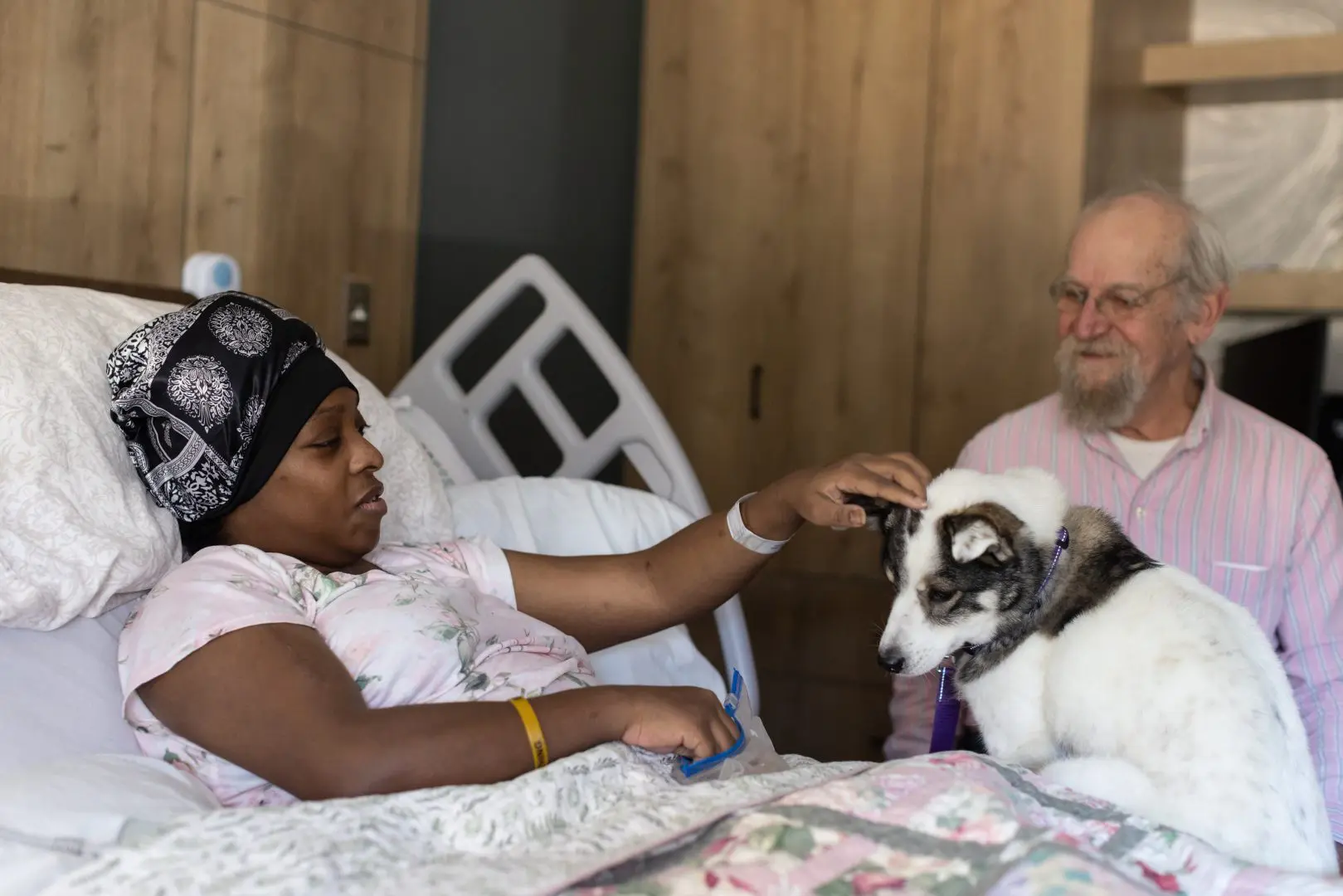 Patient in bed, petting a dog with a main sitting next to the bed