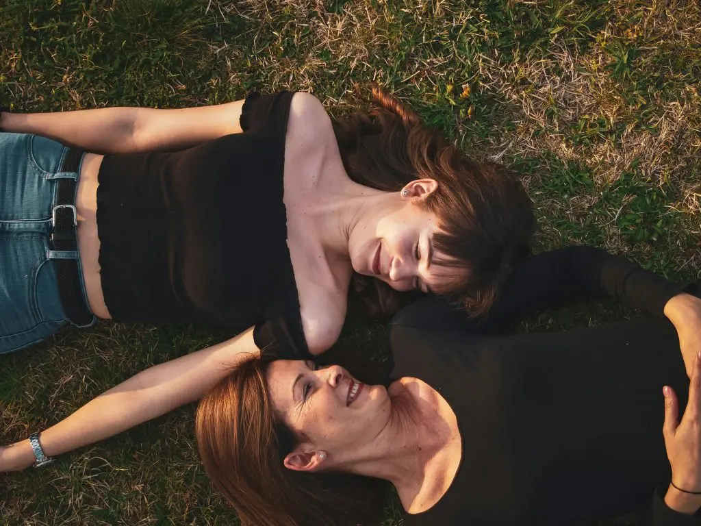 two women laying in the grass looking at each other.  Laying head to head