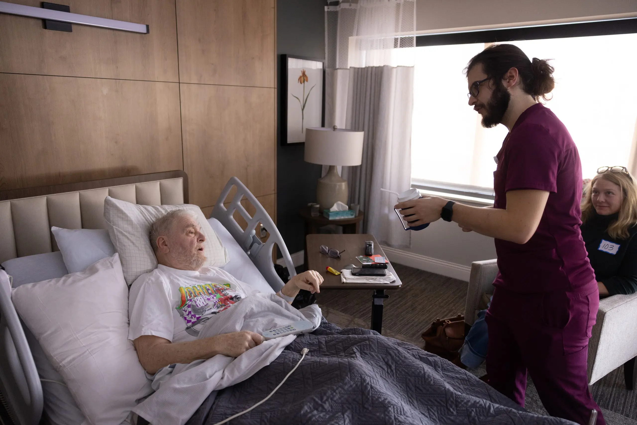 male nurse bringing a drink to a patient laying in a hospice bed
