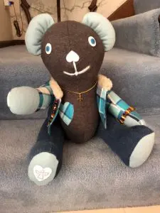 brown teddybear with cream ears and paws and a multicolored jacket with a matching heart