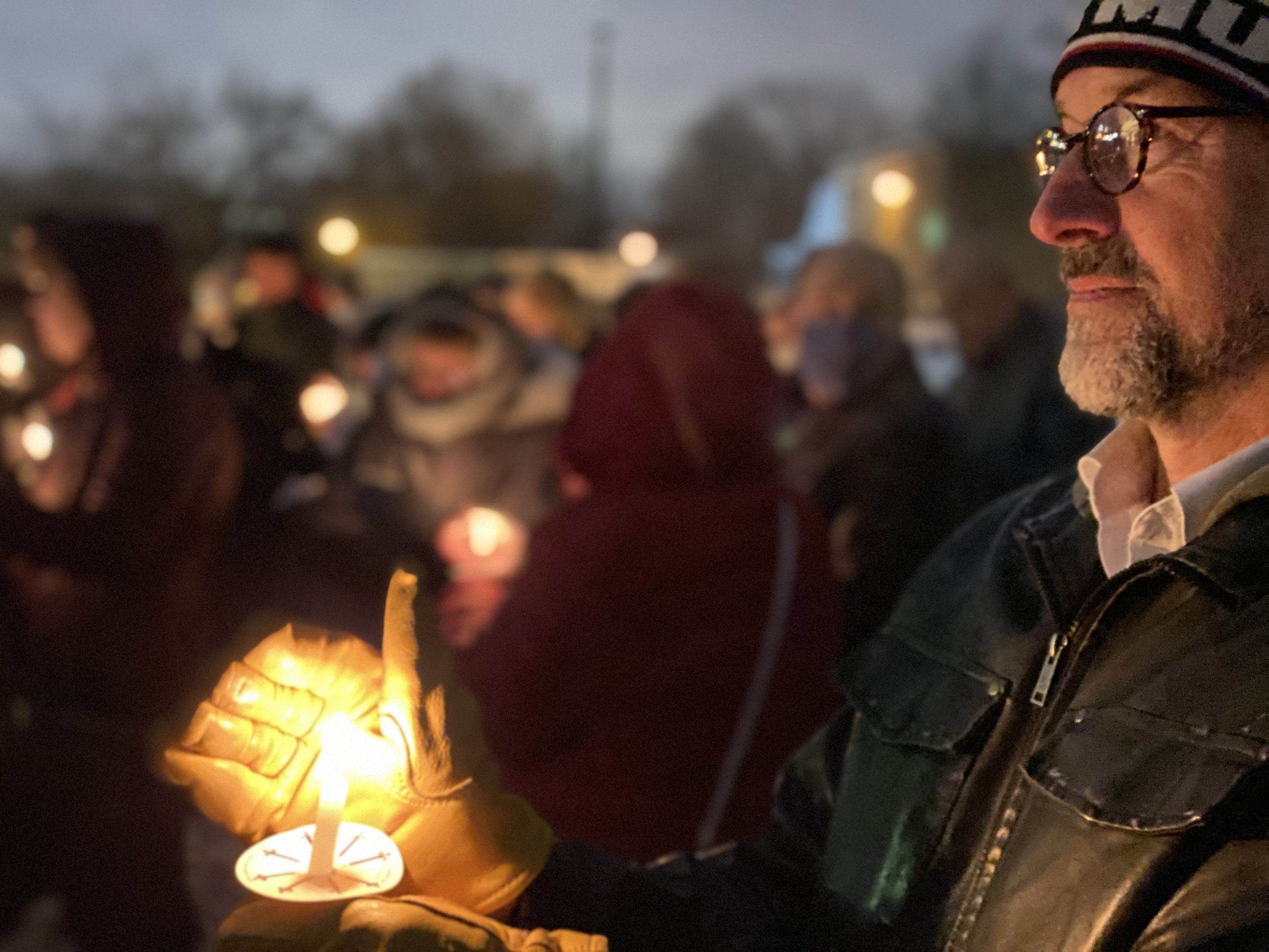 Man is standing outside with leather jacket and hat holding a candle