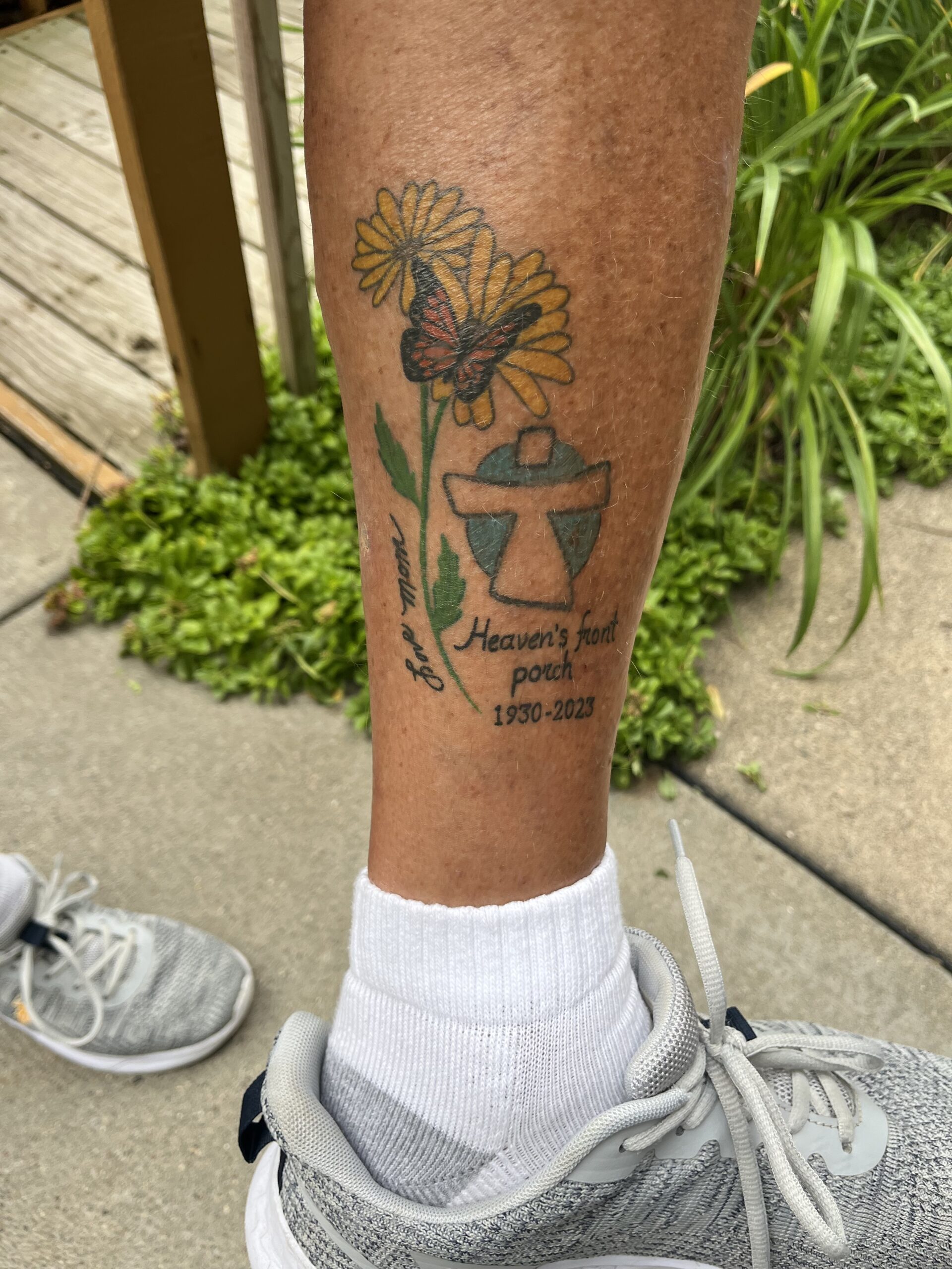 a picture of a person calf with a tattoo of a dandelion, a monarch butterfly and the Our Lady of Peace Logo with person's mothers name and Heaven's front porch 1930-2023