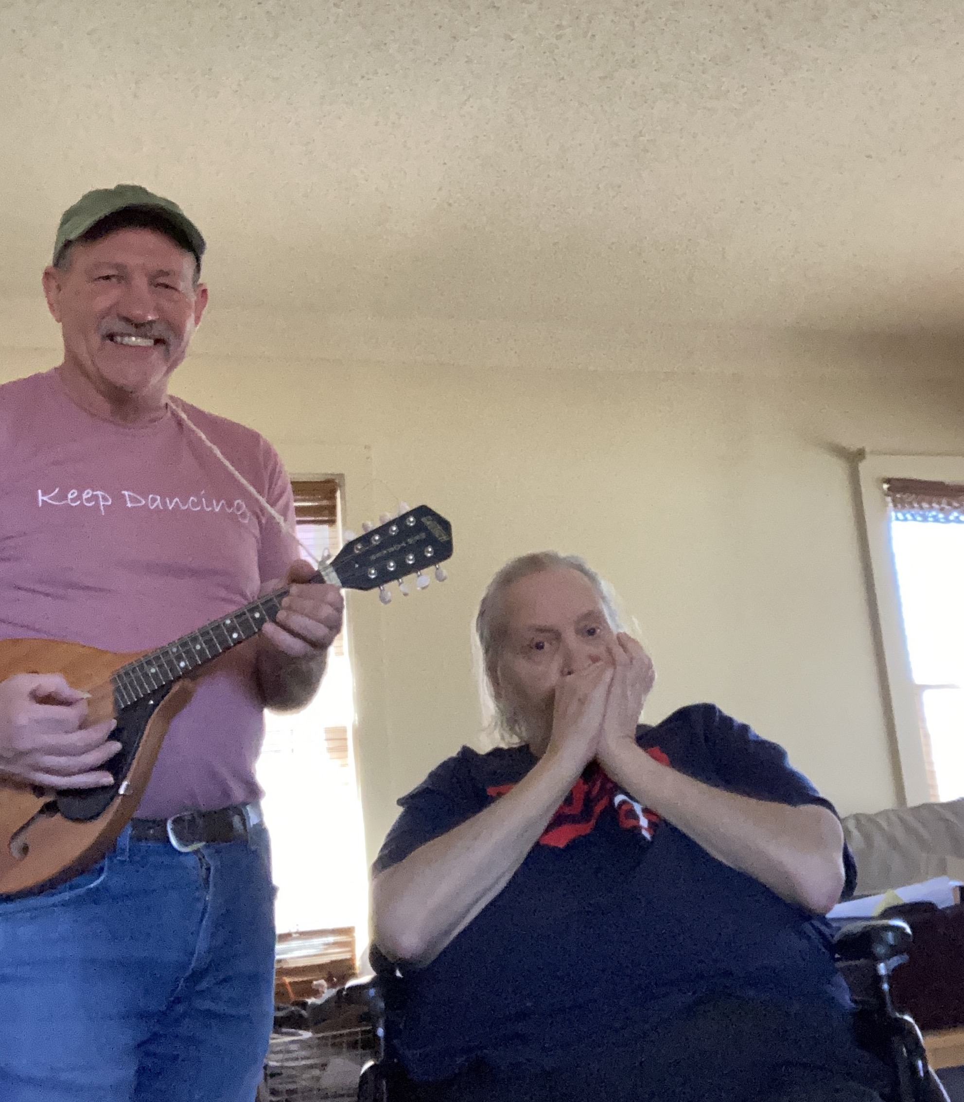 a picture of two men. One is standing playing a ukulele and the other is in a wheelchair playing a harmonica