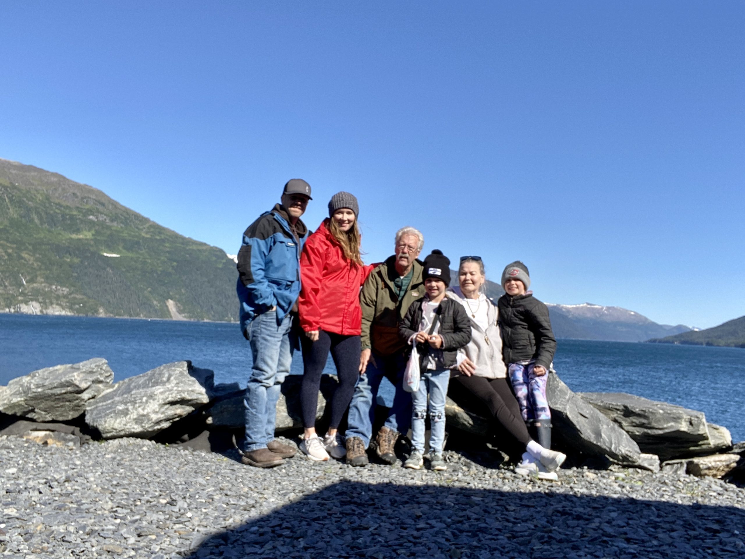 3 generation photograph on the rocks in front of the water. Mountains in the background.
