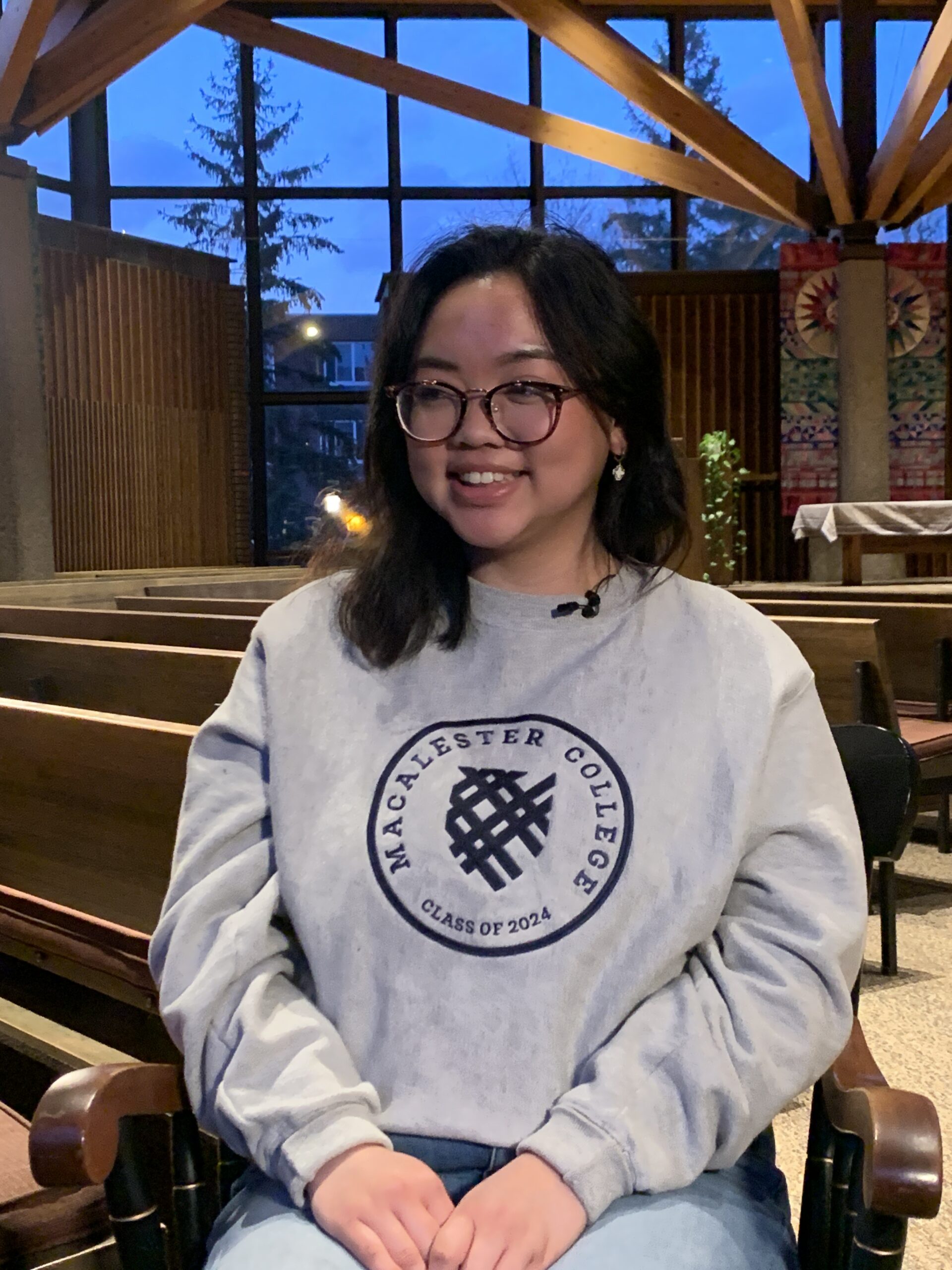 Woman wearing a Macalester College sweatshirt sitting in a chapel.