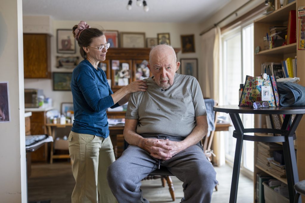 man receiving a chair massage looking into the camera. he is at his home lots of photographs hangin on the walls around him