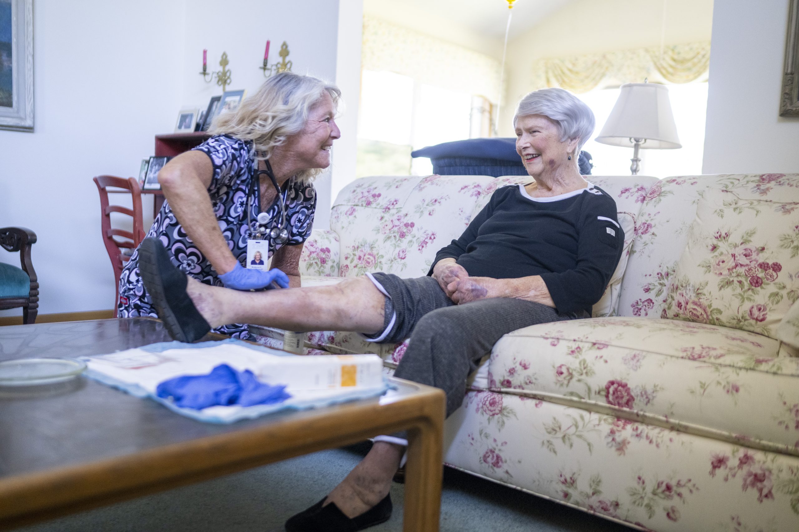 Home Health Care Nurse talking with a patient who is sitting on the couch getting a leg massage